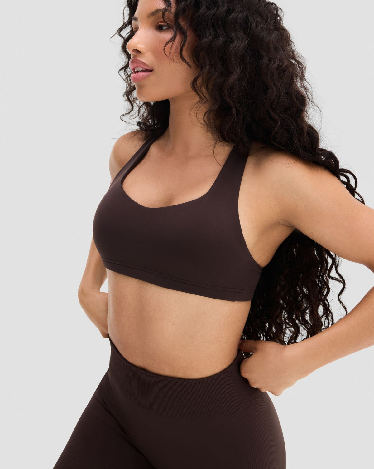 Elevate Sculpting Medium Impact Multiway Bra in Coffee Brown, three-quarter front view of scoop neckline, hands on hips